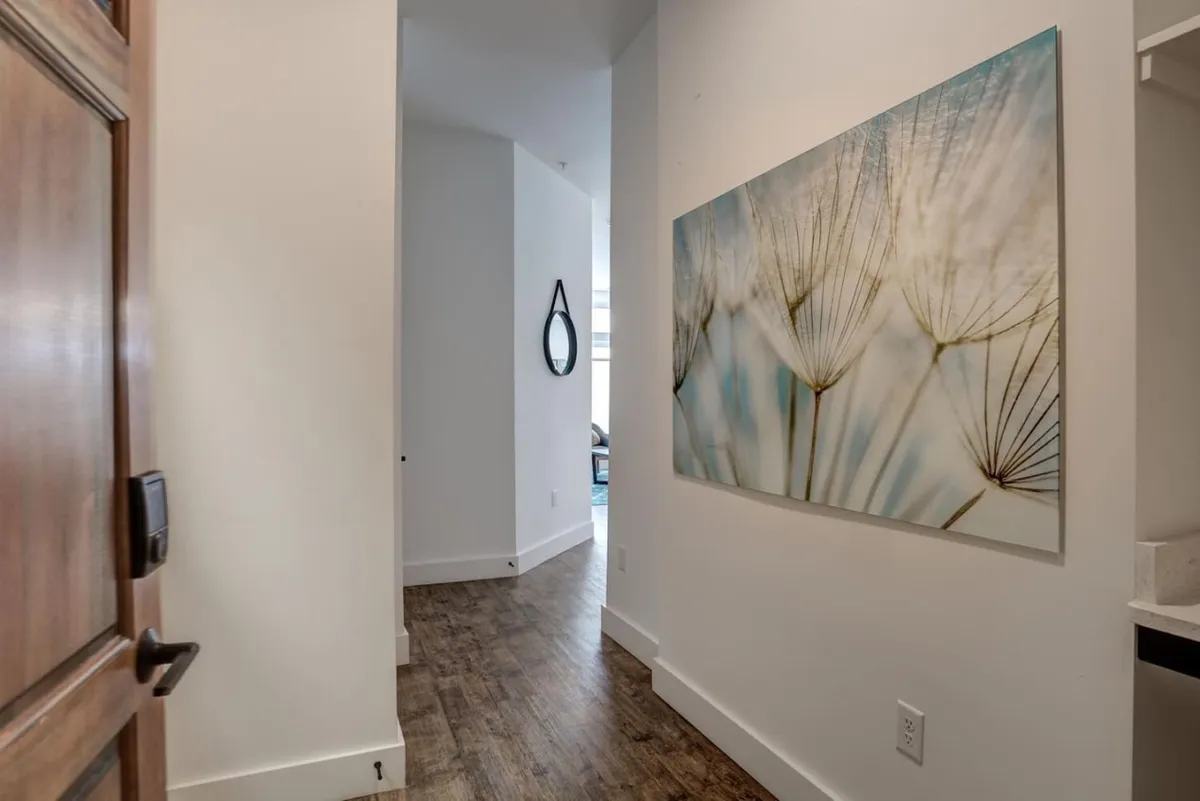 This interior image captures the entryway of the condo, featuring stylish artwork on the wall, a mirror, and a doorway leading into another room. The scene suggests a welcoming atmosphere as guests enter and begin their experience in the home.