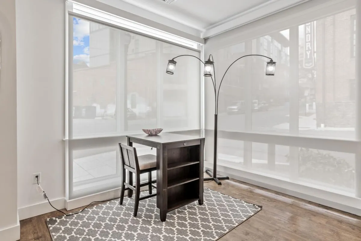 A well-lit table and chair setup stands beside a floor lamp, creating an inviting and practical workspace. The scene is thoughtfully arranged for reading, working on a laptop, or enjoying a quiet coffee, with subtle touches that suggest both productivity and comfort.