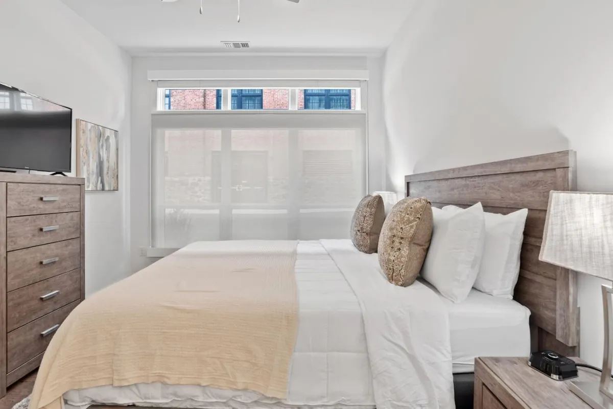 This image showcases a beautiful king bed with plush, decorative pillows, a sleek dresser, a television, and a window that fills the room with natural light. The overall setting is serene and cozy, capturing the atmosphere of a restful retreat.