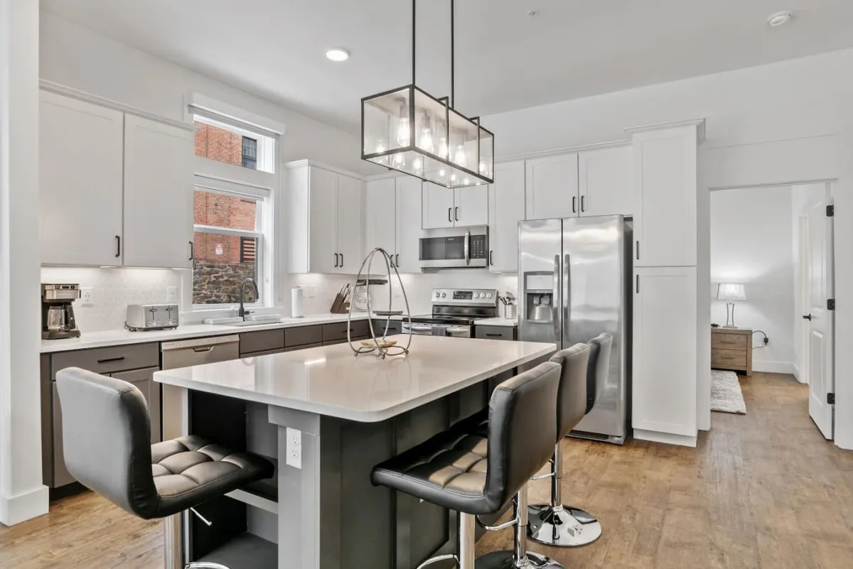 An open-layout kitchen with a large island countertop, stylish light fixture, and gleaming stainless steel appliances. The design is both functional and inviting, with space for meal prep, entertaining, and everyday family moments.