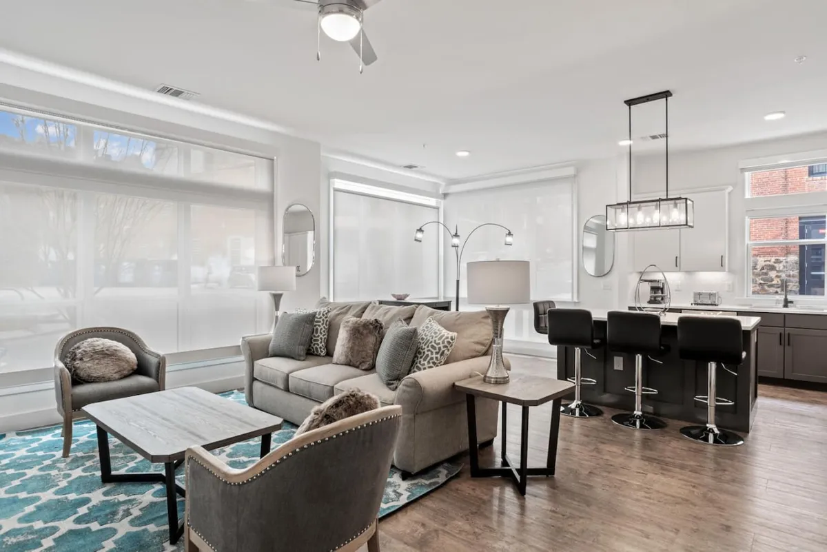 A cozy living space anchored by a contemporary sofa, area rug, and kitchen island in the background. The lighting fixtures and clear sightlines between living and kitchen areas highlight the integrated, open layout. The arrangement is ideal for relaxing, entertaining, or enjoying a movie night on the queen sofa bed.