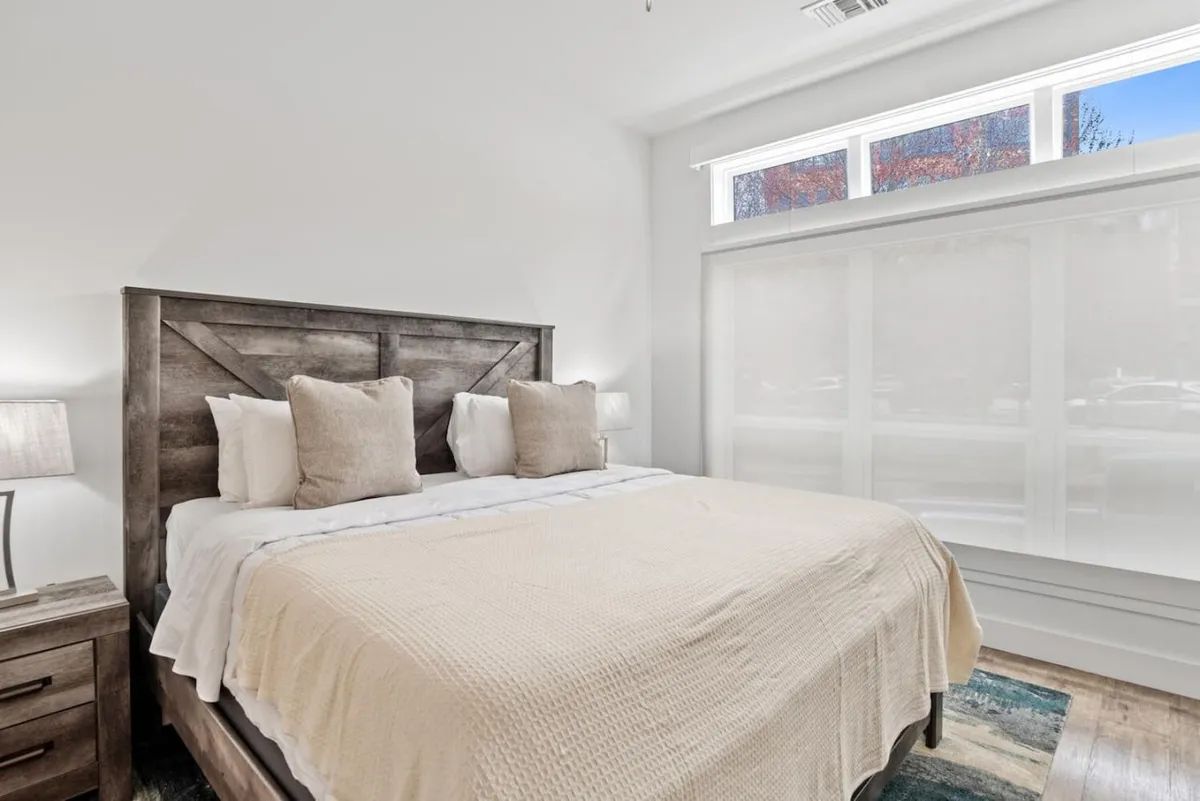 A bright, peaceful bedroom featuring a well-made bed with soft bedding, nightstands topped with modern lamps, and large windows letting in abundant natural light. The setting invites relaxation and comfort, ideal for restorative rest after a productive workday.